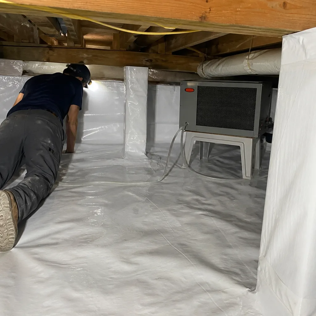 Technician inspecting crawl space encapsulation with vapor barrier and dehumidifier